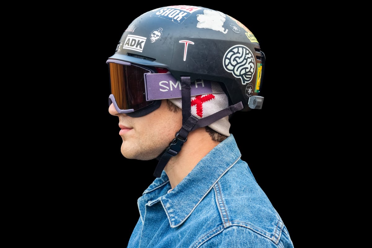 A skier in goggles, in profile, with a Noggin sensor on the back of a sticker-covered helmet
