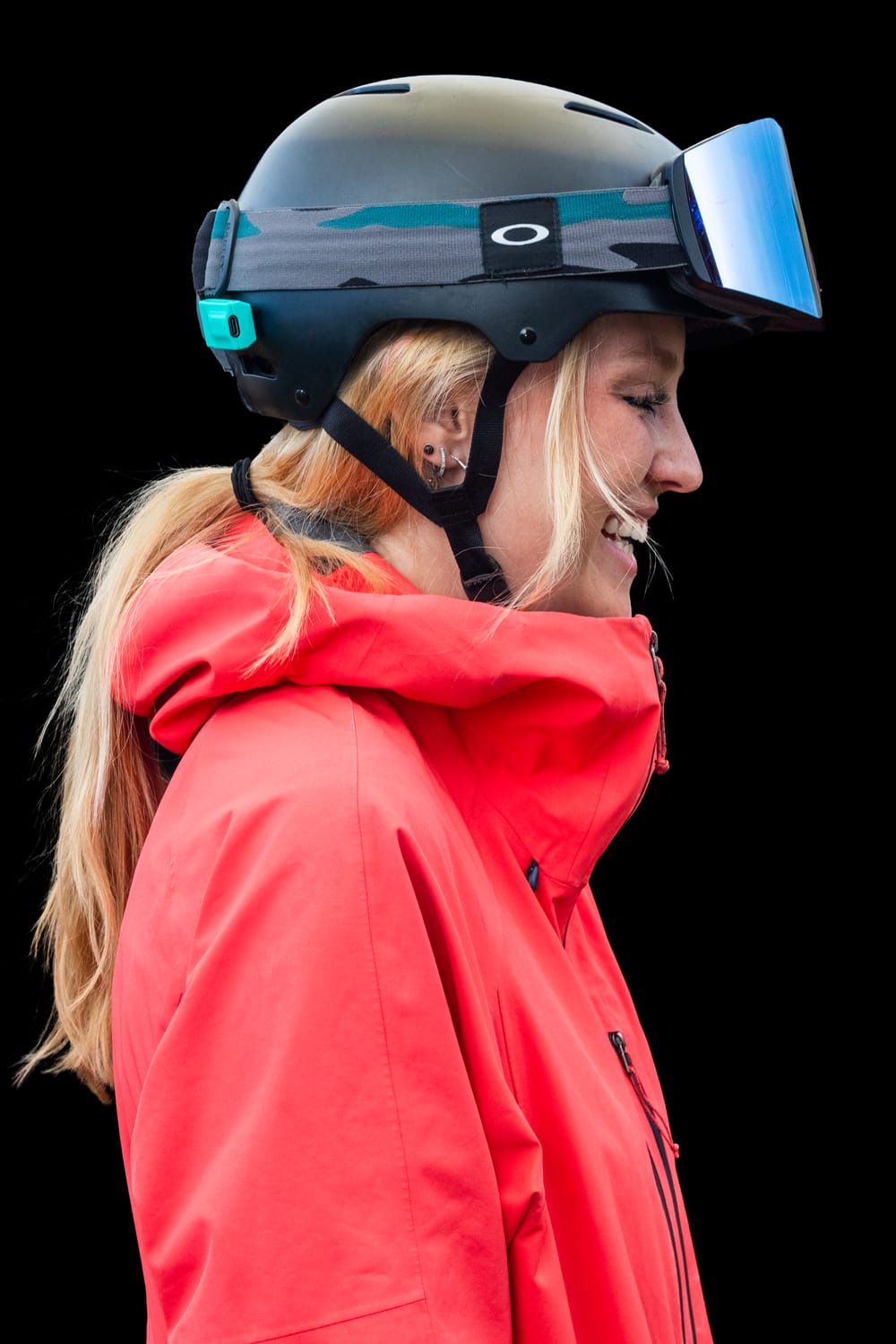 A smiling skier in a red jacket, in profile, with a Noggin sensor on the back of the helmet